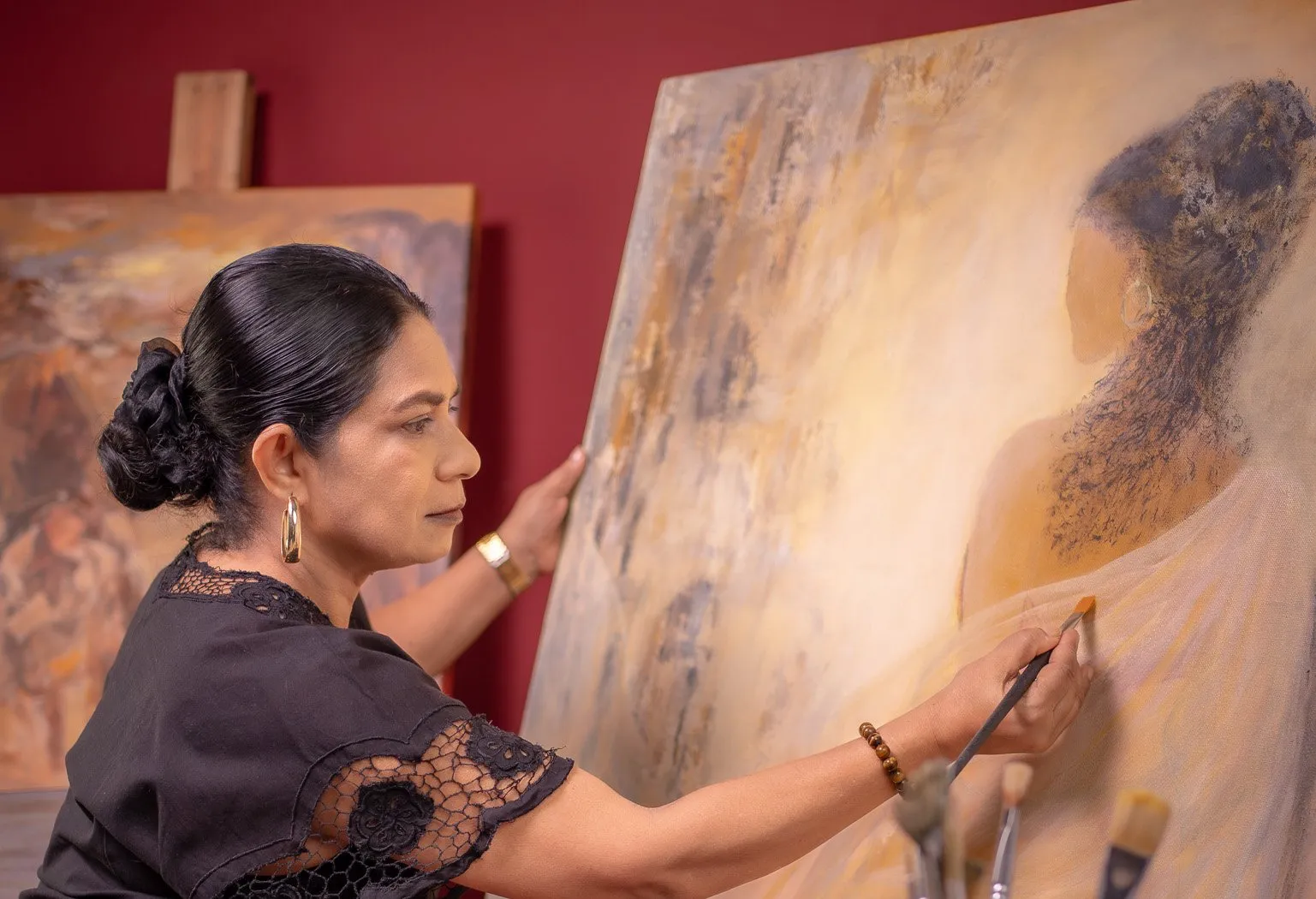 Priyadarshani Tennakoon painting in the studio, one hand steadying the canvas